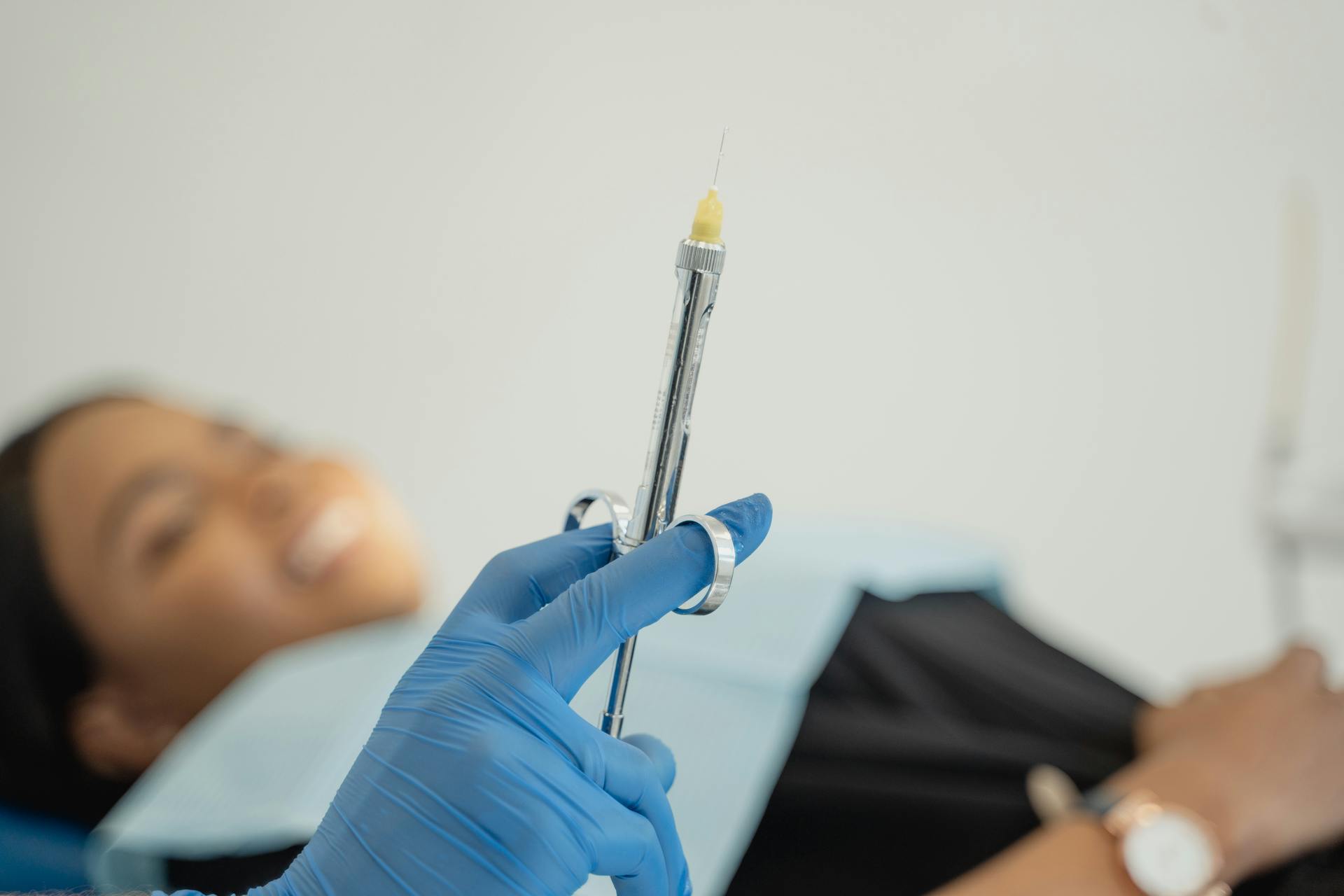 A dentist holding a syringe with patient in background, showcasing dental procedure readiness.