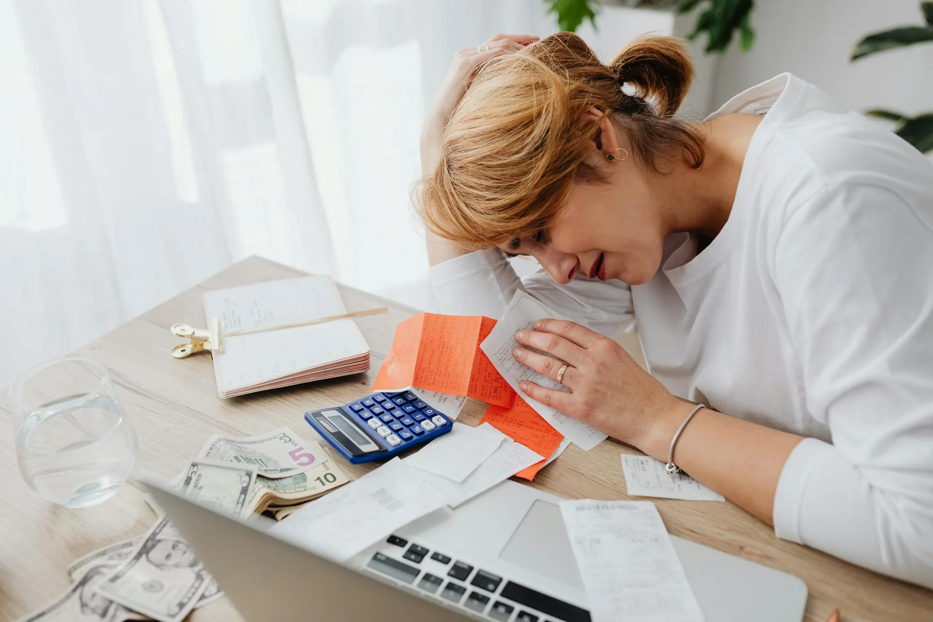 Stressed business owner reviewing finances, receipts, and cash at a desk