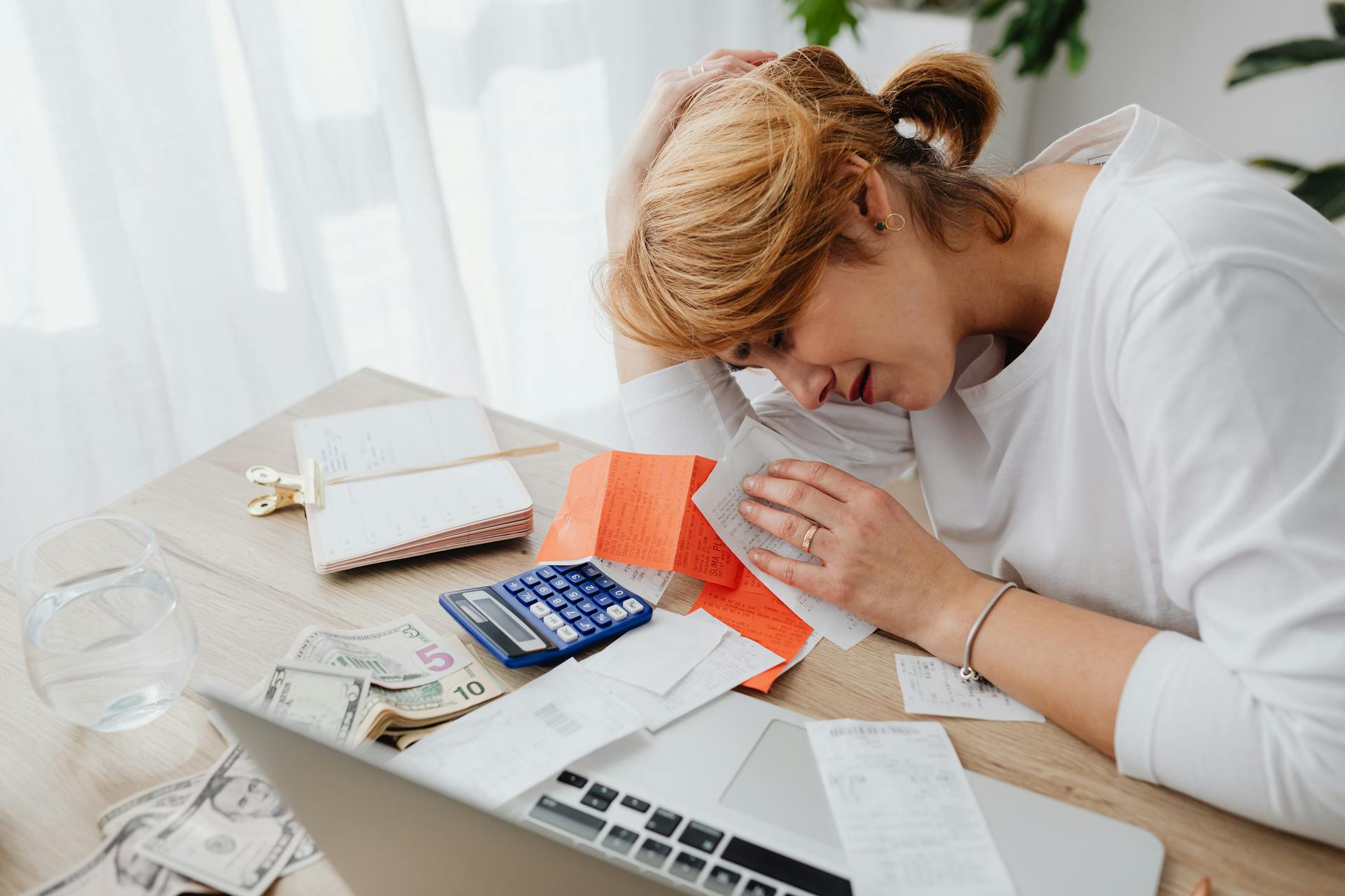 Stressed business owner reviewing finances, receipts, and cash at a desk